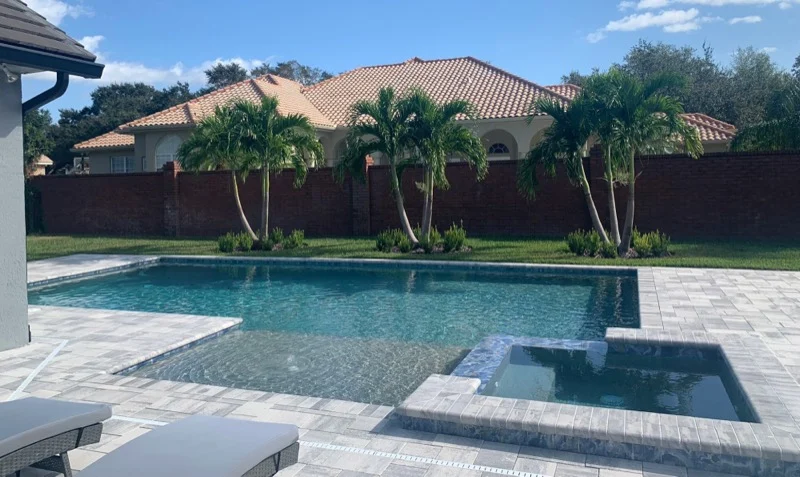 Custom pool and raised spa behind a Mediterranean-style Central Florida home, with travertine decking and mature palms